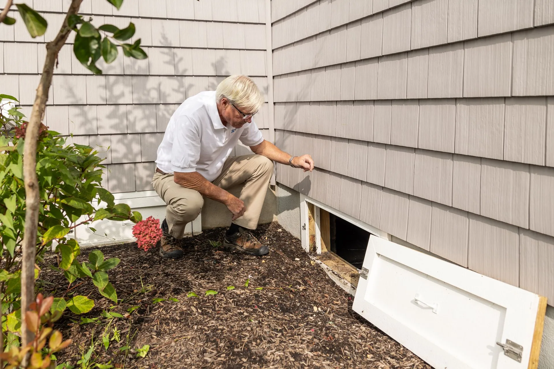 Inspector checking a crawl space opening on a house foundation before designing a radon system