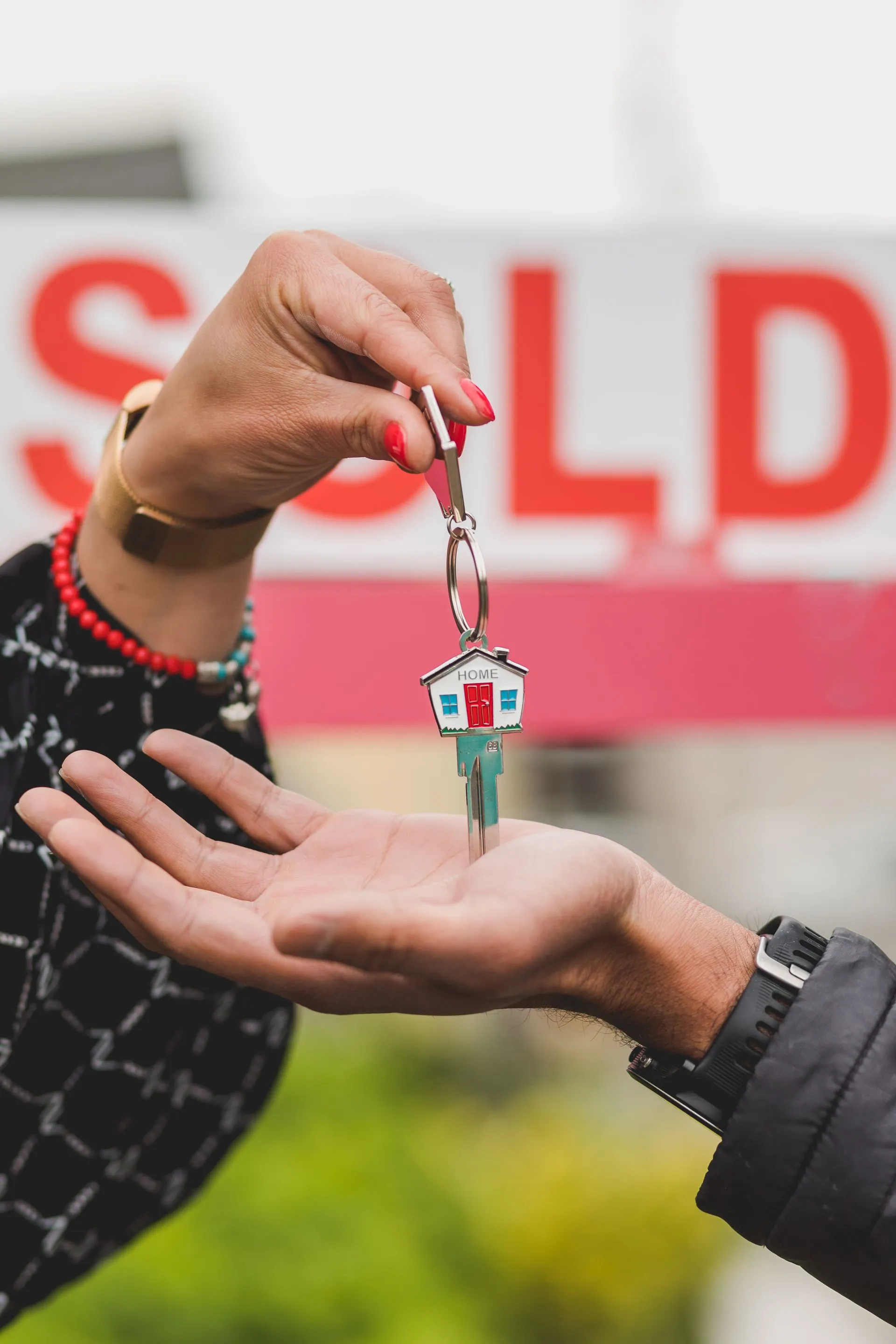 House key handed over in front of a SOLD sign after a home sale